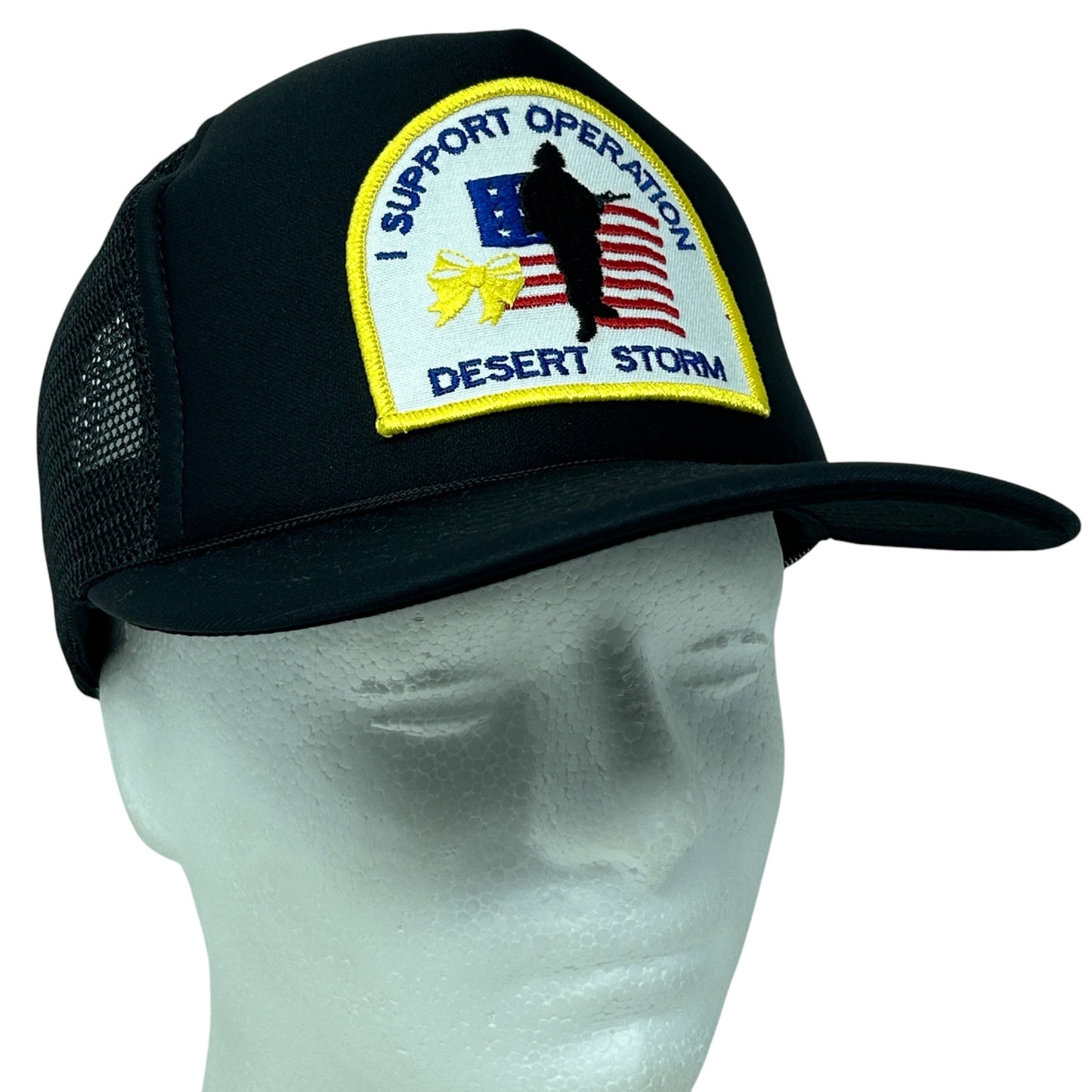 Black mesh trucker hat with yellow embroidery supporting Operation Desert Storm, featuring front patch and adjustable fit.