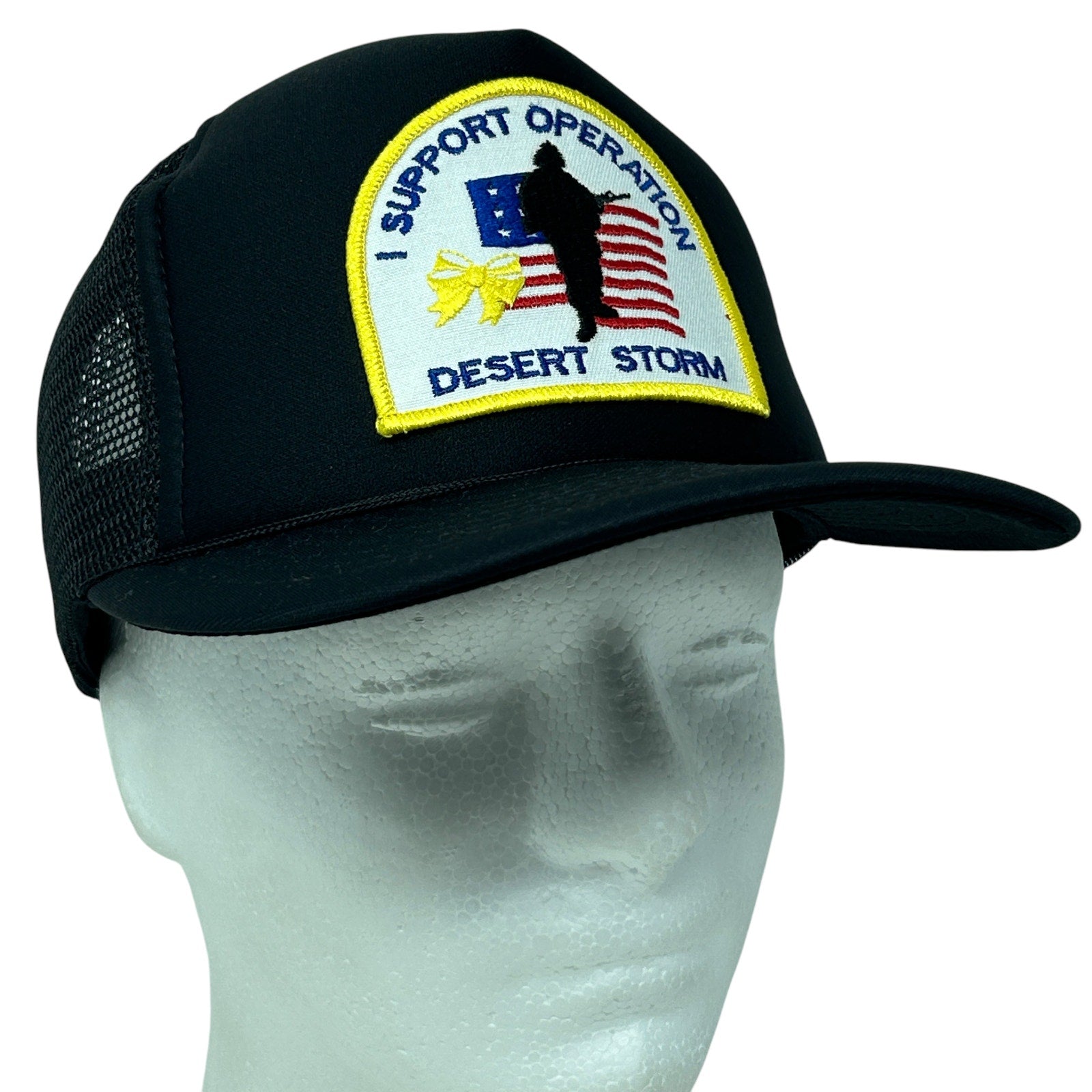 Black mesh trucker hat with yellow embroidery supporting Operation Desert Storm, featuring front patch and adjustable fit.