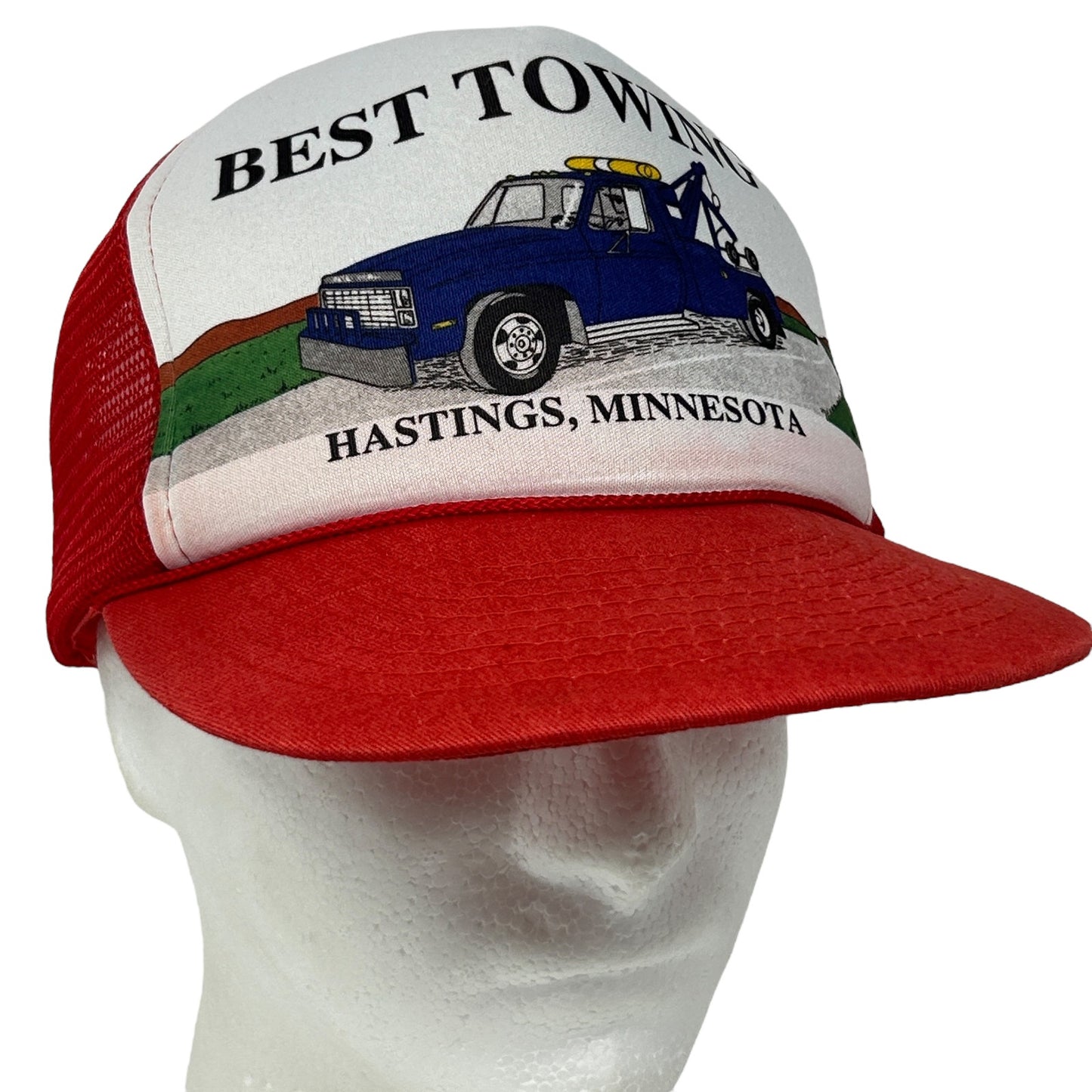 Vintage red trucker hat featuring a tow truck graphic and 'Best Towing Hastings, Minnesota' logo on the front