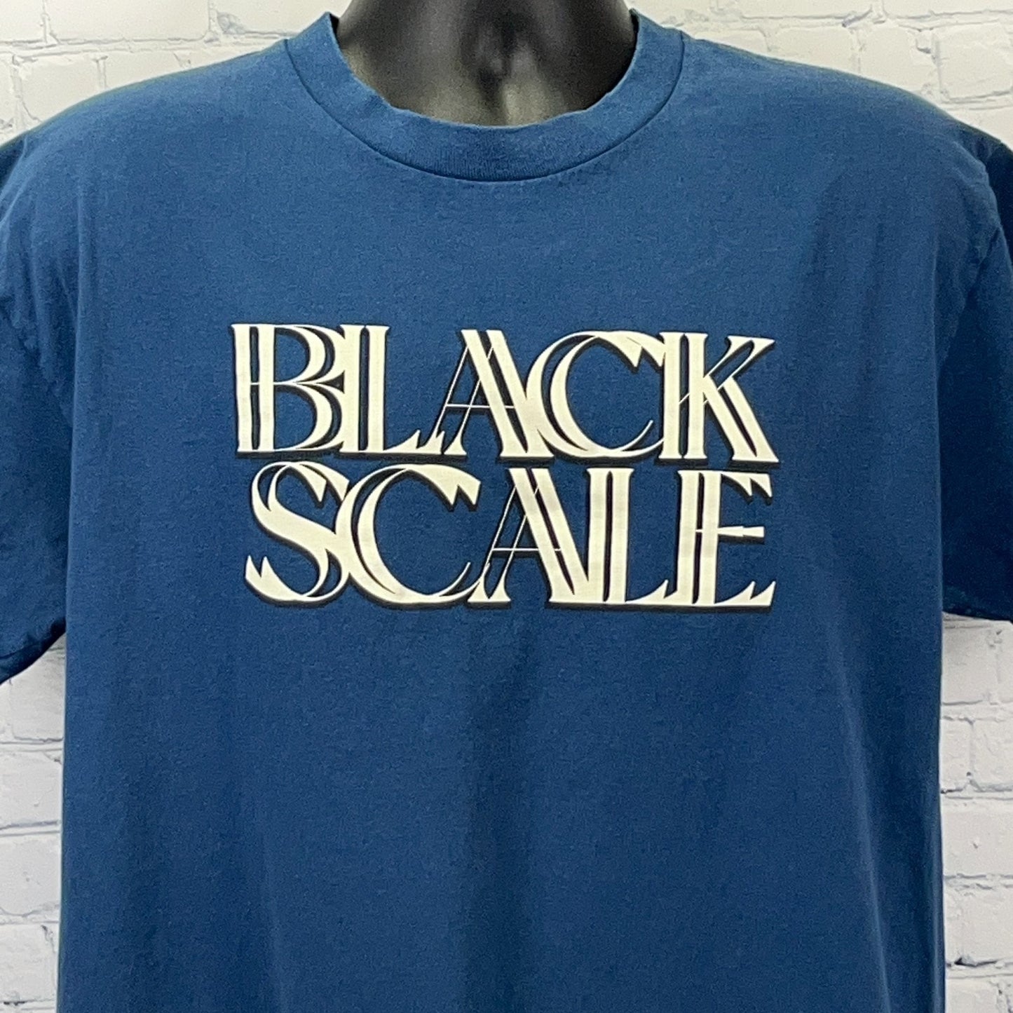 Front view of a blue Black Scale t-shirt featuring bold white logo print