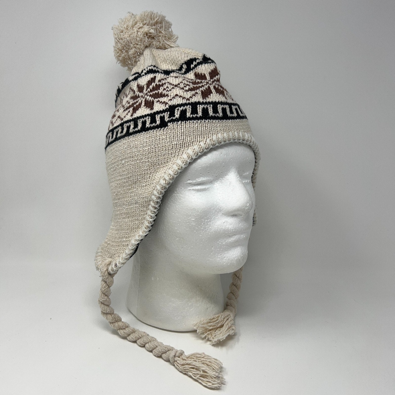 Unbranded beige beanie with pom-pom, ear flaps, and tribal pattern, shown on a mannequin head