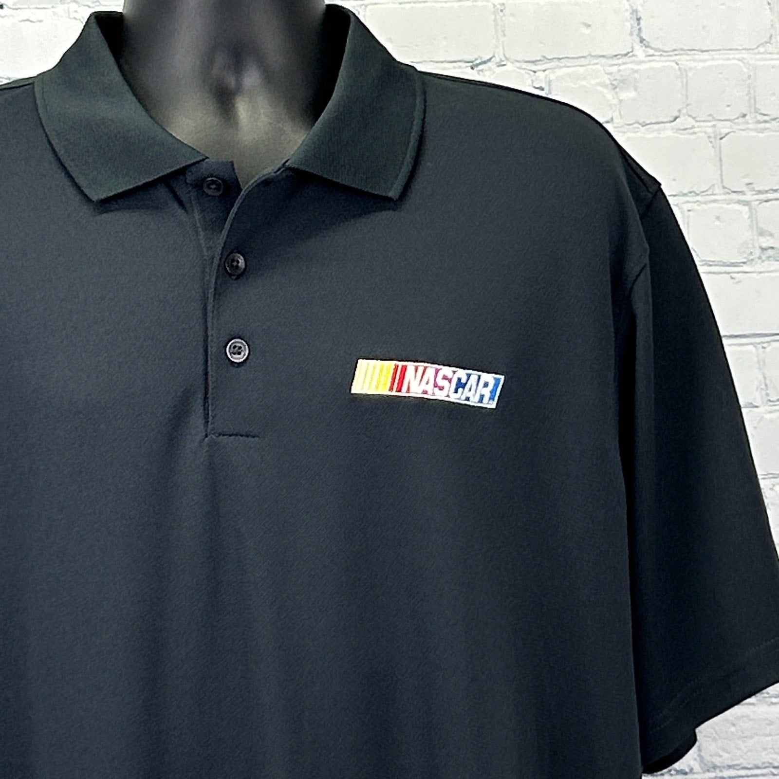 Black NASCAR Polo by Antigua with embroidered logo on the front, displayed on a mannequin