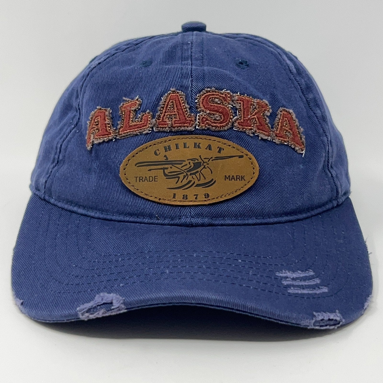 Front view of a blue unbranded cap featuring a distressed 'Alaska' logo and leather patch
