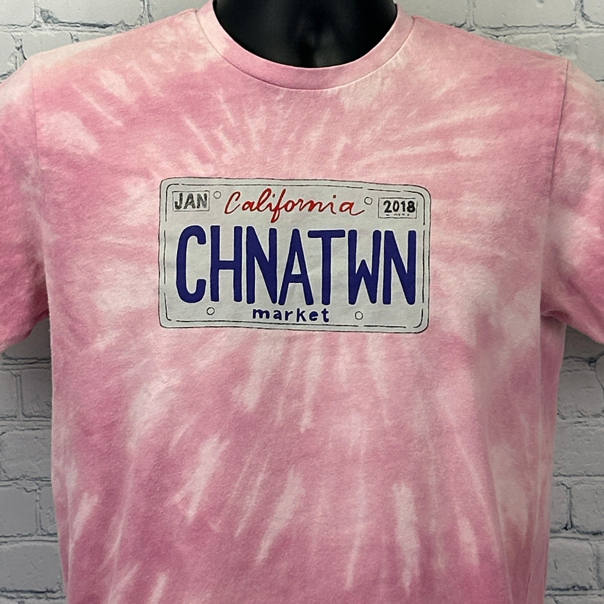 Front view of pink tie-dye T-shirt by Chinatown Market Studios with California license plate graphic