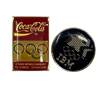 Coca-Cola Olympic sponsor pin in red and gold with Olympic rings and IBM logo in gold on black background
