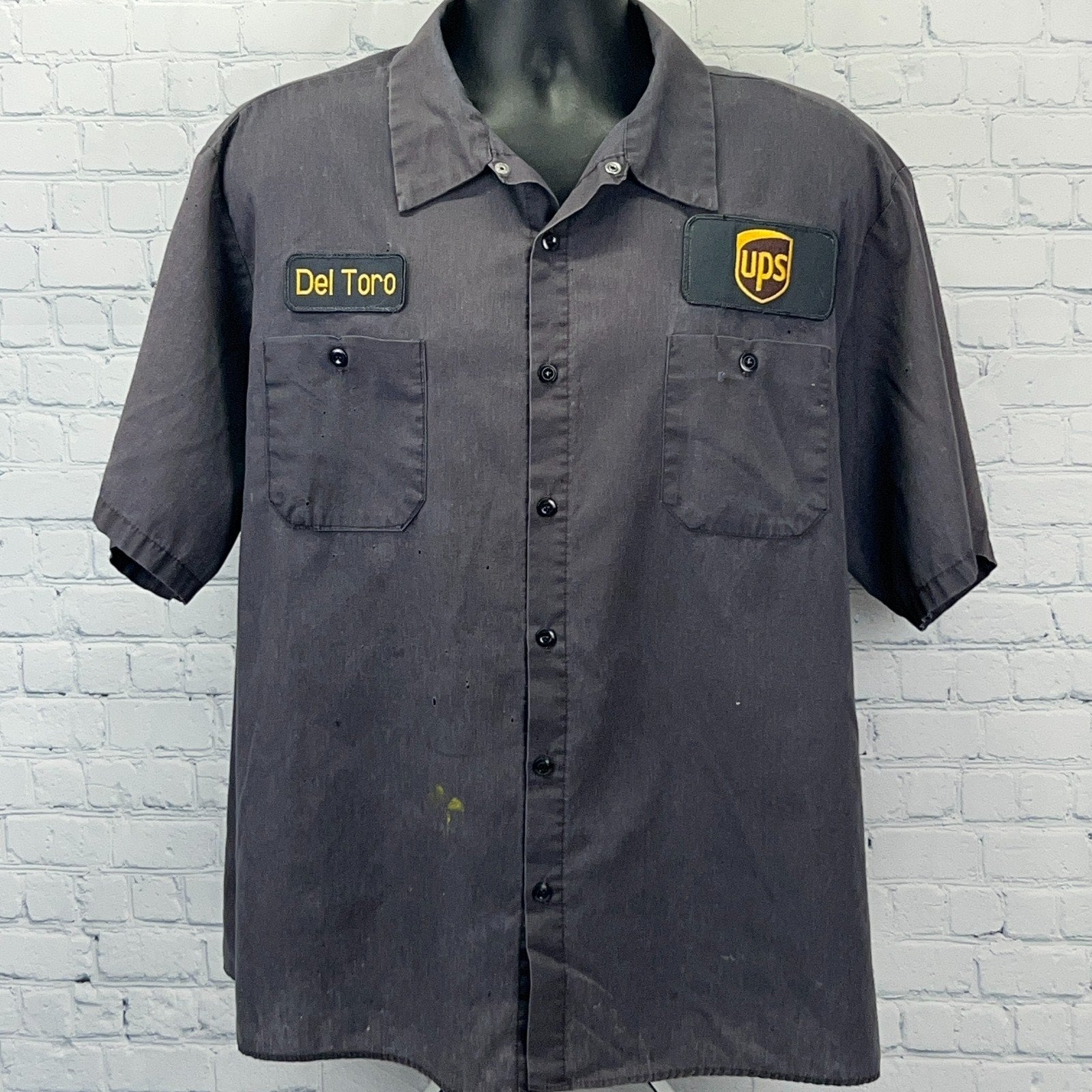 Black short-sleeve uniform shirt from Aramark with UPS logo and Del Toro embroidered name patch on front