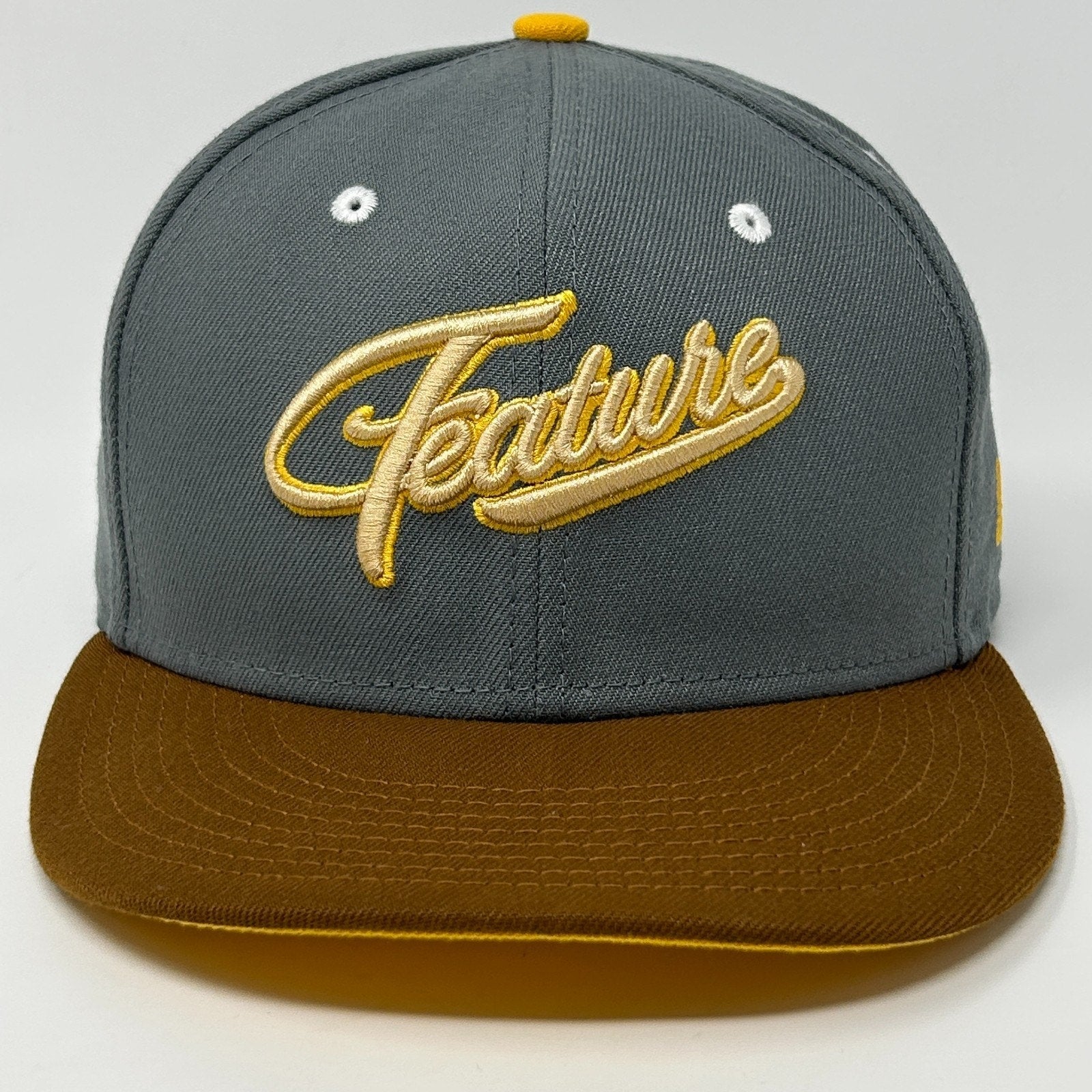 Gray New Era hat with brown visor and yellow 'Feature' embroidery on the front