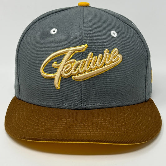 Gray New Era hat with brown visor and yellow 'Feature' embroidery on the front