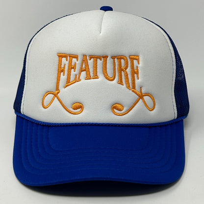 Front view of blue and white Feature Hat with orange embroidered logo on a trucker style cap
