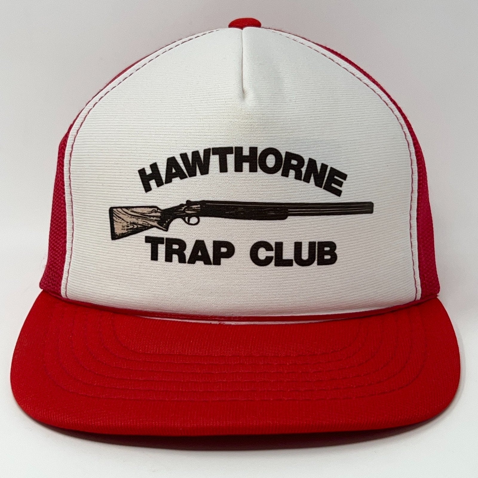 Front view of a red and white trucker cap hat featuring Hawthorne Trap Club logo with a shotgun graphic