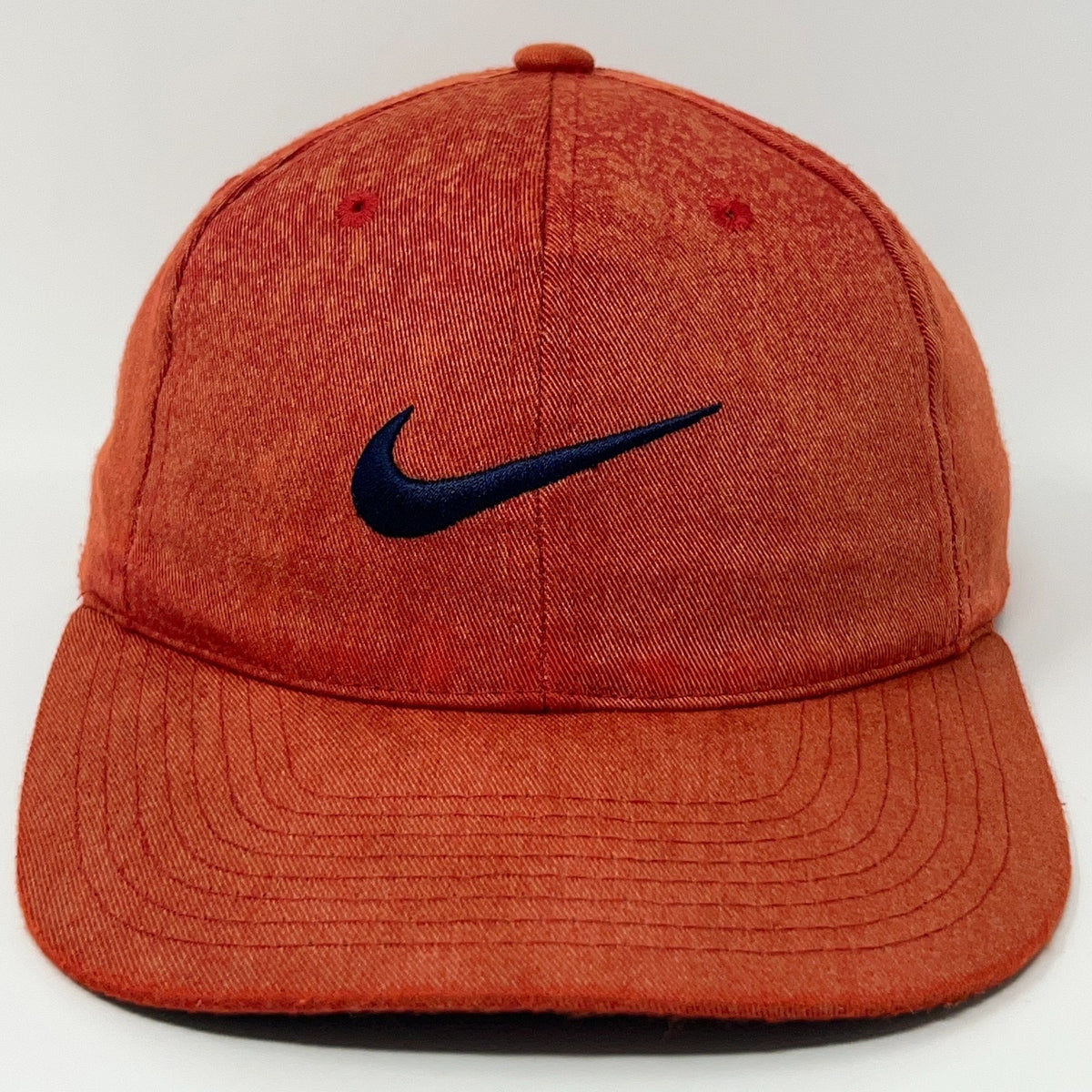 Nike cap in orange with a dark blue Nike logo on the front, showcasing a relaxed fit style.