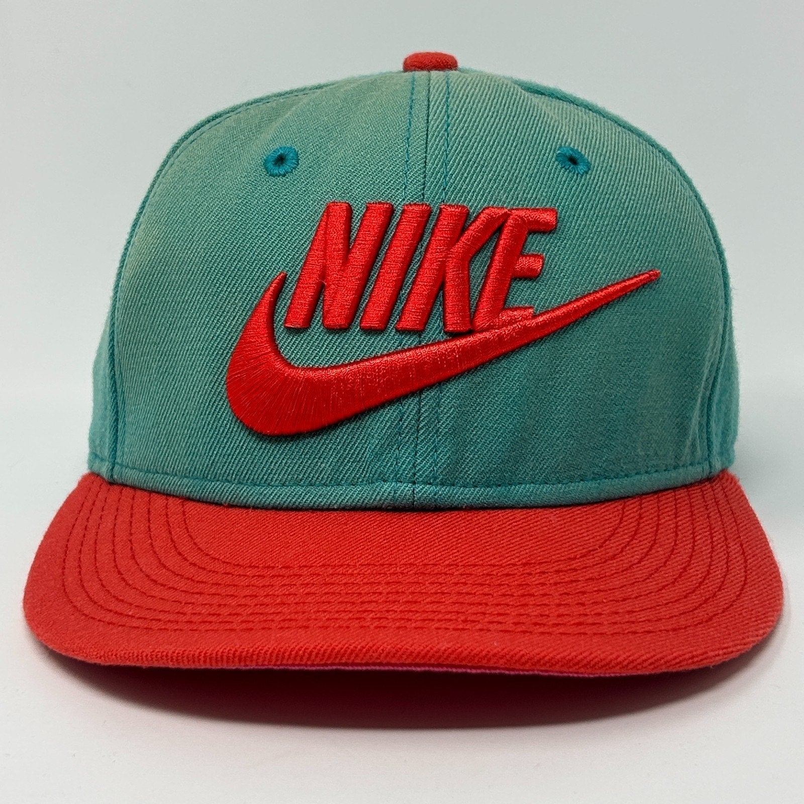 Front view of Nike teal and red snapback hat featuring bold Nike logo and contrasting visor