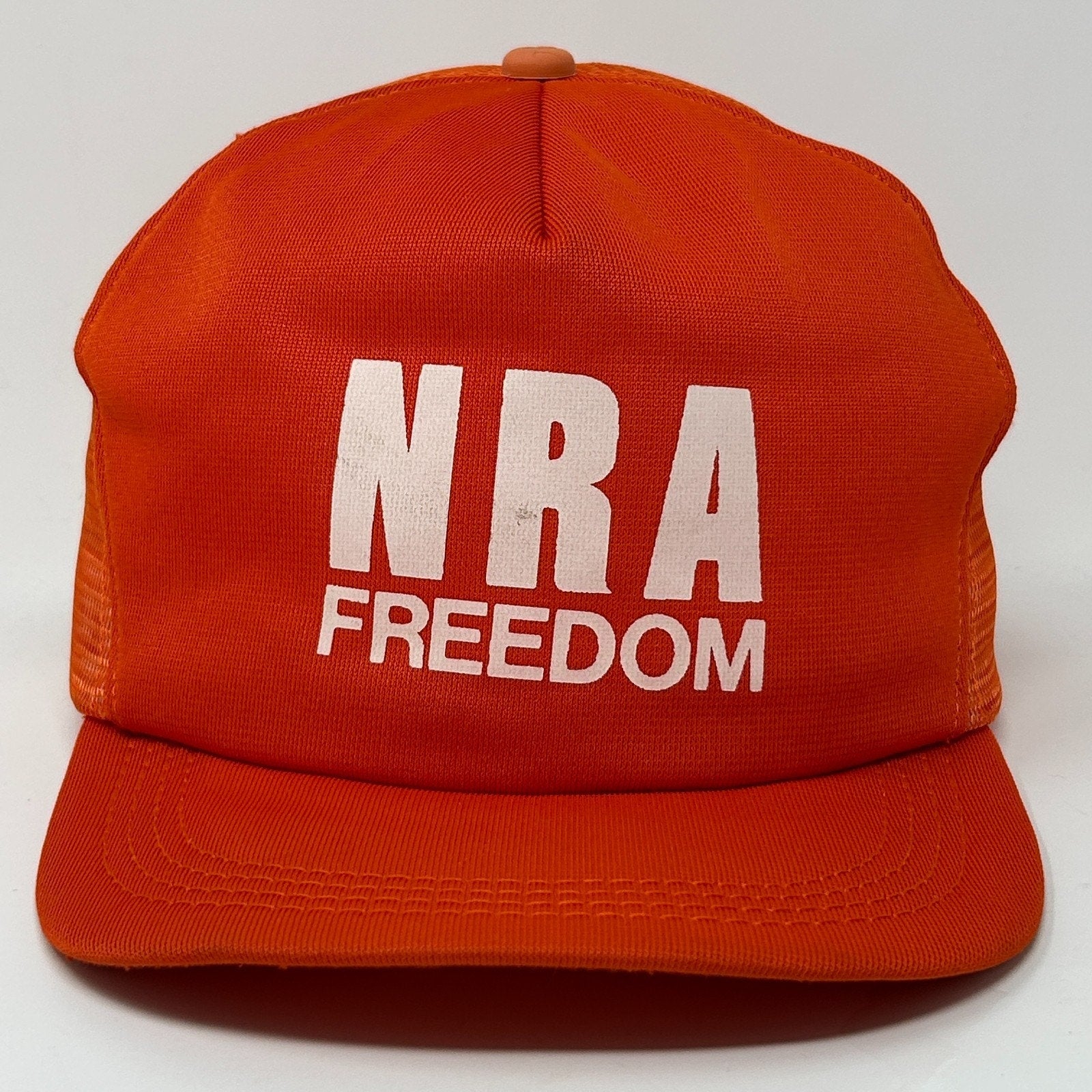 NRA Trucker Hat in vibrant orange featuring bold white 'NRA FREEDOM' text on the front