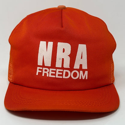 NRA Trucker Hat in vibrant orange featuring bold white 'NRA FREEDOM' text on the front