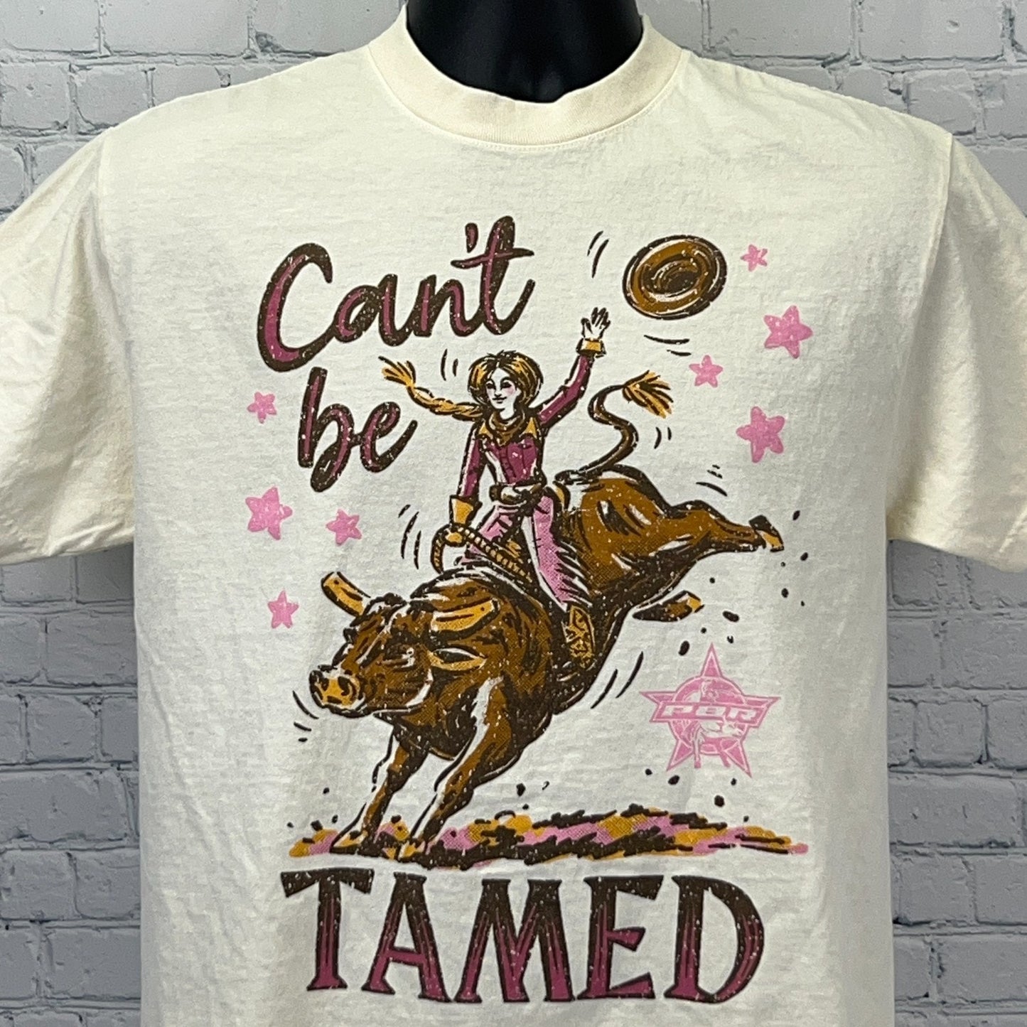 Cream PBR Professional Bull Riders T-shirt with graphic of a cowgirl taming a bull