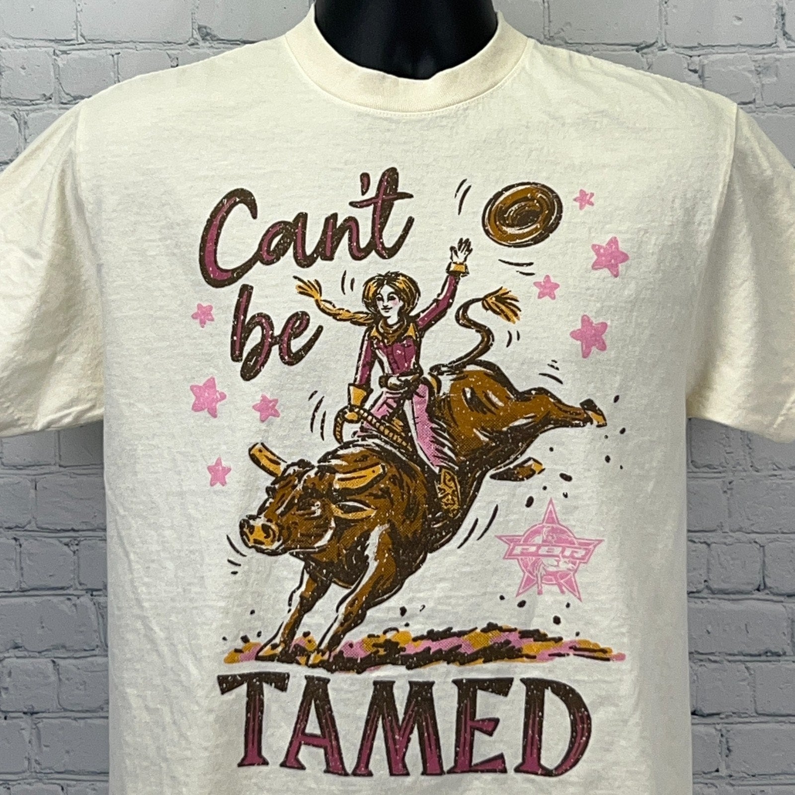Cream PBR Professional Bull Riders T-shirt with graphic of a cowgirl taming a bull