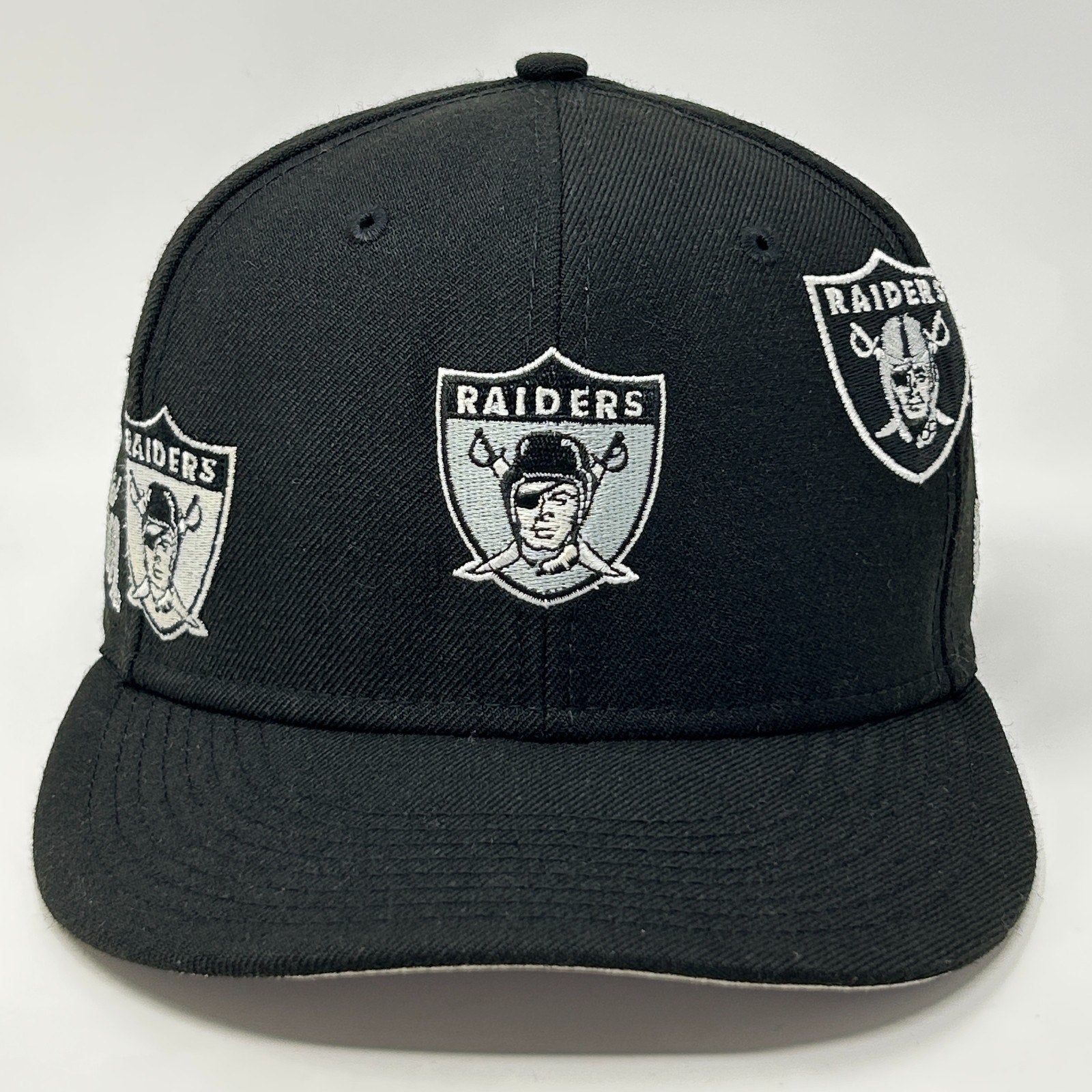 Black New Era Raiders Hat featuring multiple embroidered team logos on the front view.