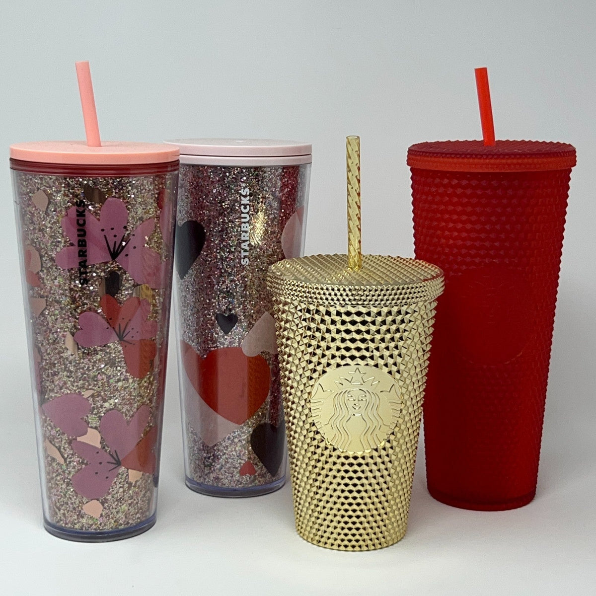 Starbucks colorful tumblers in pink, red, and gold with unique designs and reusable straws