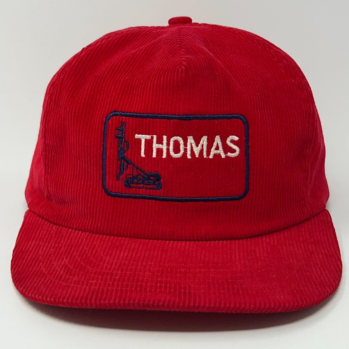 Red corduroy cap with Thomas Drilling Equipment logo, featuring a vintage design