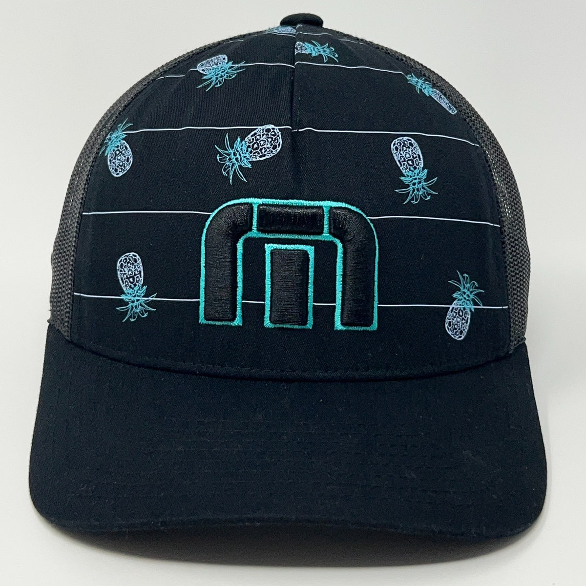 TravisMathew black trucker hat with blue pineapple pattern and distinctive logo