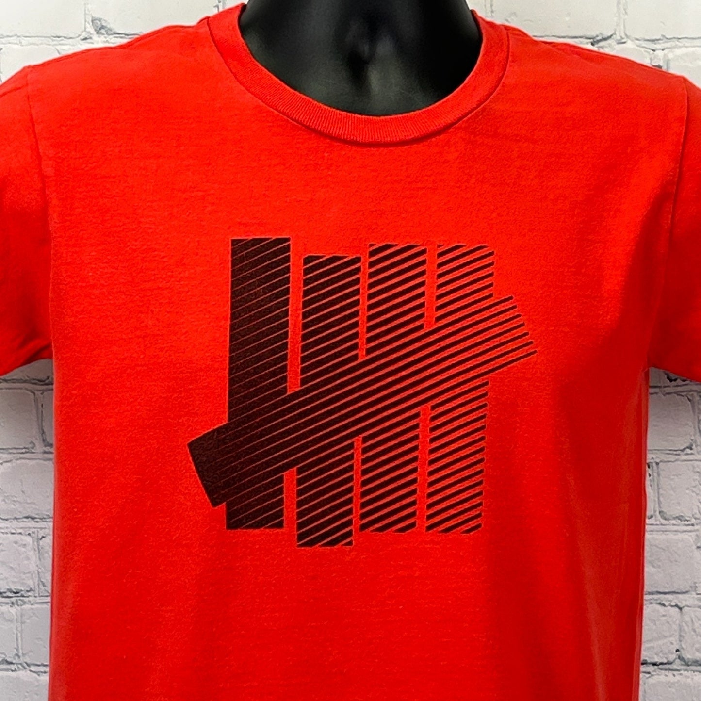 Undefeated T Shirt in red featuring black striped logo on the front for a bold look