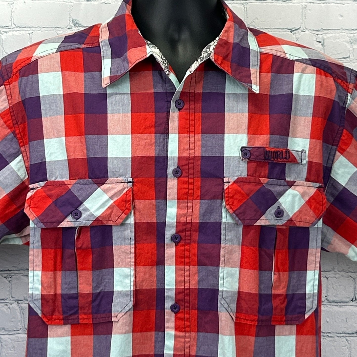 Front view of a World Industries Shirt in red, blue and purple plaid with pockets and logo detailing