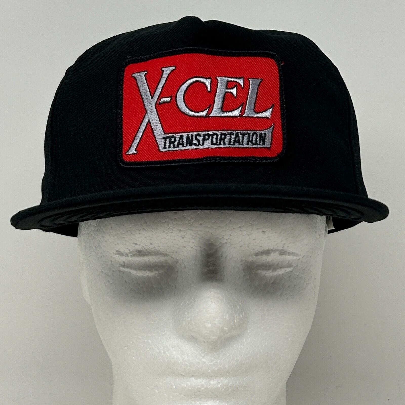 Front view of black DeLong hat featuring X-Cel Transportation logo in red and white for a bold look